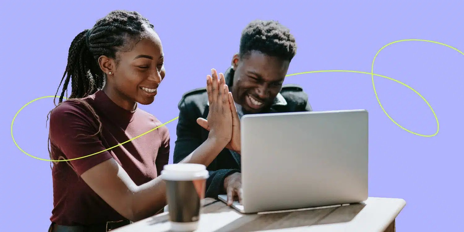Male and female coworkers high five in front of laptop